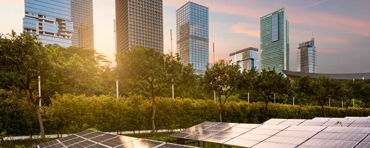 Comunità energetiche rinnovabili. Grattacieli al tramonto sullo sfondo e pannelli fotovoltaici in primo piano.