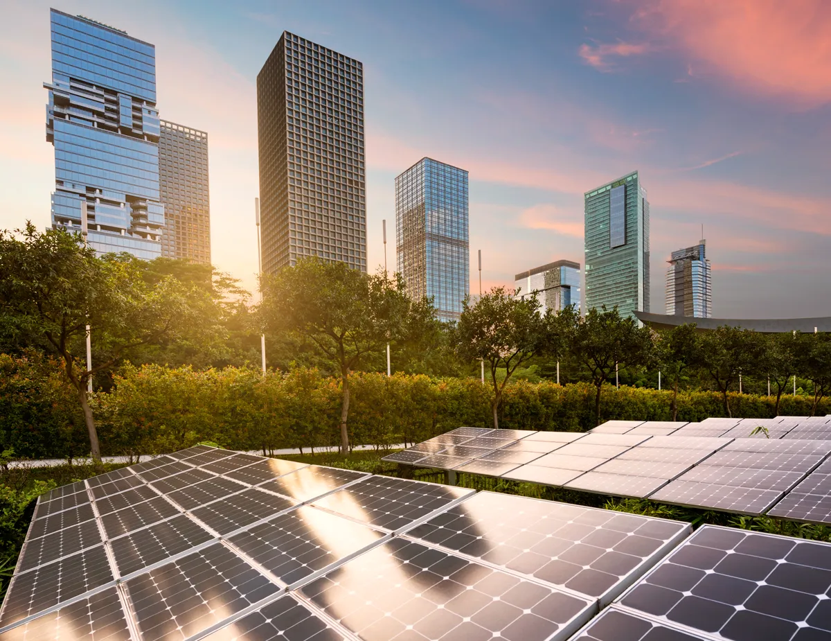 Comunità energetiche rinnovabili. Grattacieli al tramonto sullo sfondo e pannelli fotovoltaici in primo piano.